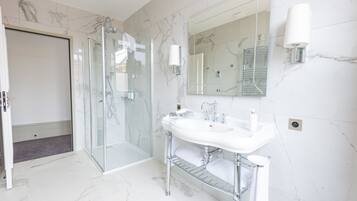 A modern bathroom with a glass shower enclosure, a white sink with chrome fixtures, and a large mirror with wall sconces.