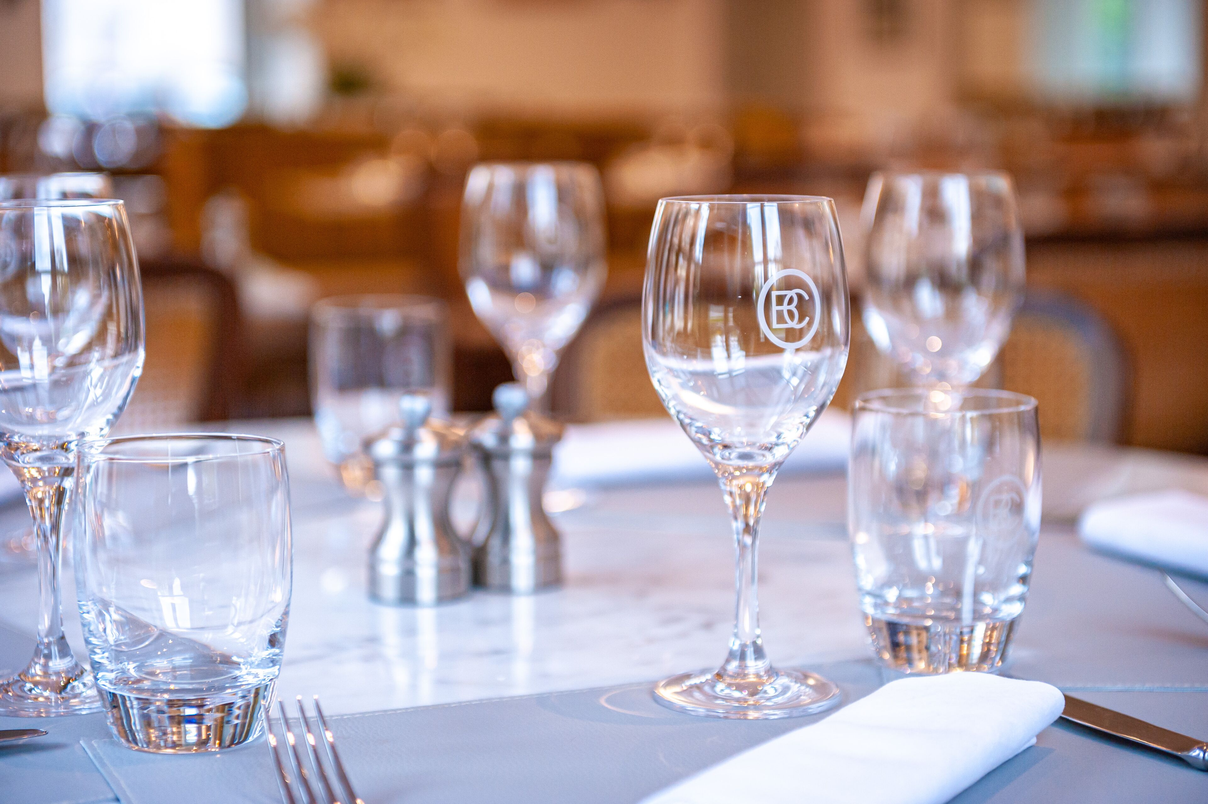 Una mesa de comedor dispuesta con copas de vino transparentes, un vaso de agua y un salero y pimentero.