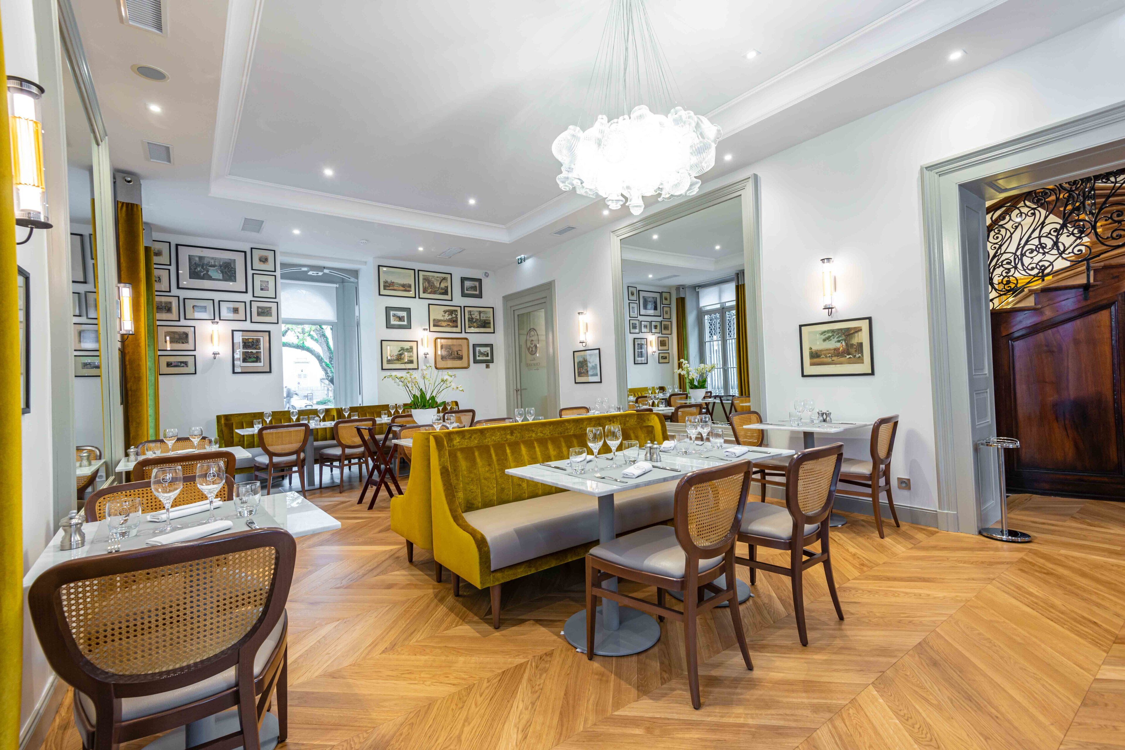 A restaurant with wooden flooring, yellow cushioned seating, and framed pictures on the walls.