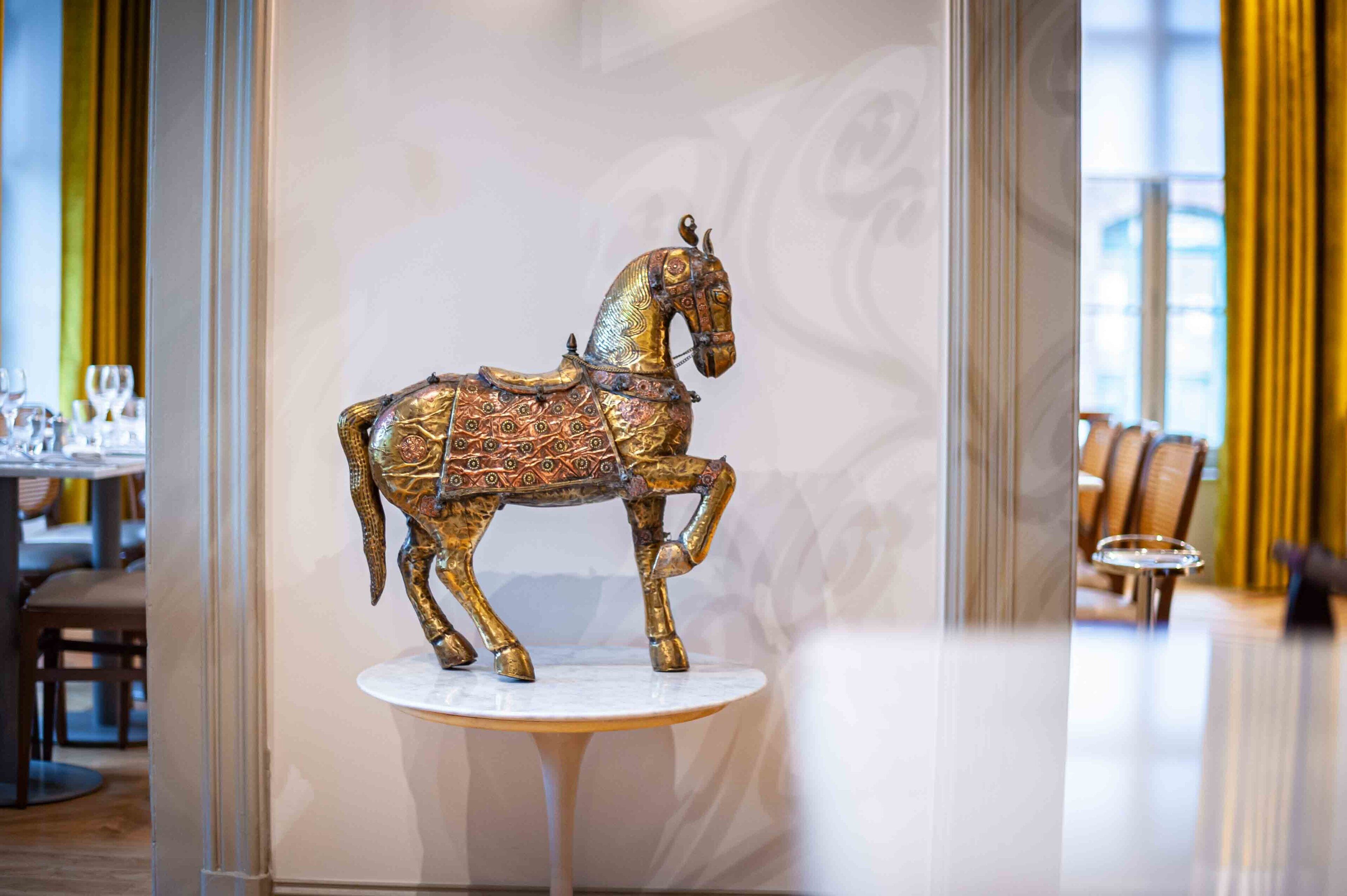 A decorative horse statue on a pedestal in a well-lit room with a modern interior design.