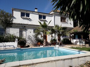 Un edificio blanco con piscina, rodeado de palmeras y plantas en macetas.