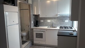 Cocina compacta con armarios blancos, horno integrado, lavamanos y estufa.