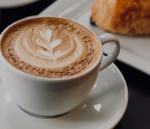 A cup of coffee with latte art on a saucer. - Hotel Jägerhof Wörthersee - Only Adults Official Partner Amoria Spa (Krumpendorf am Woerther See)