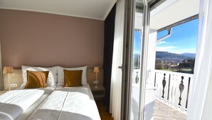 A hotel room with two beds, a balcony with a view of the countryside, and a window with curtains. - Hotel Jägerhof Wörthersee - Only Adults Official Partner Amoria Spa (Krumpendorf am Woerther See)