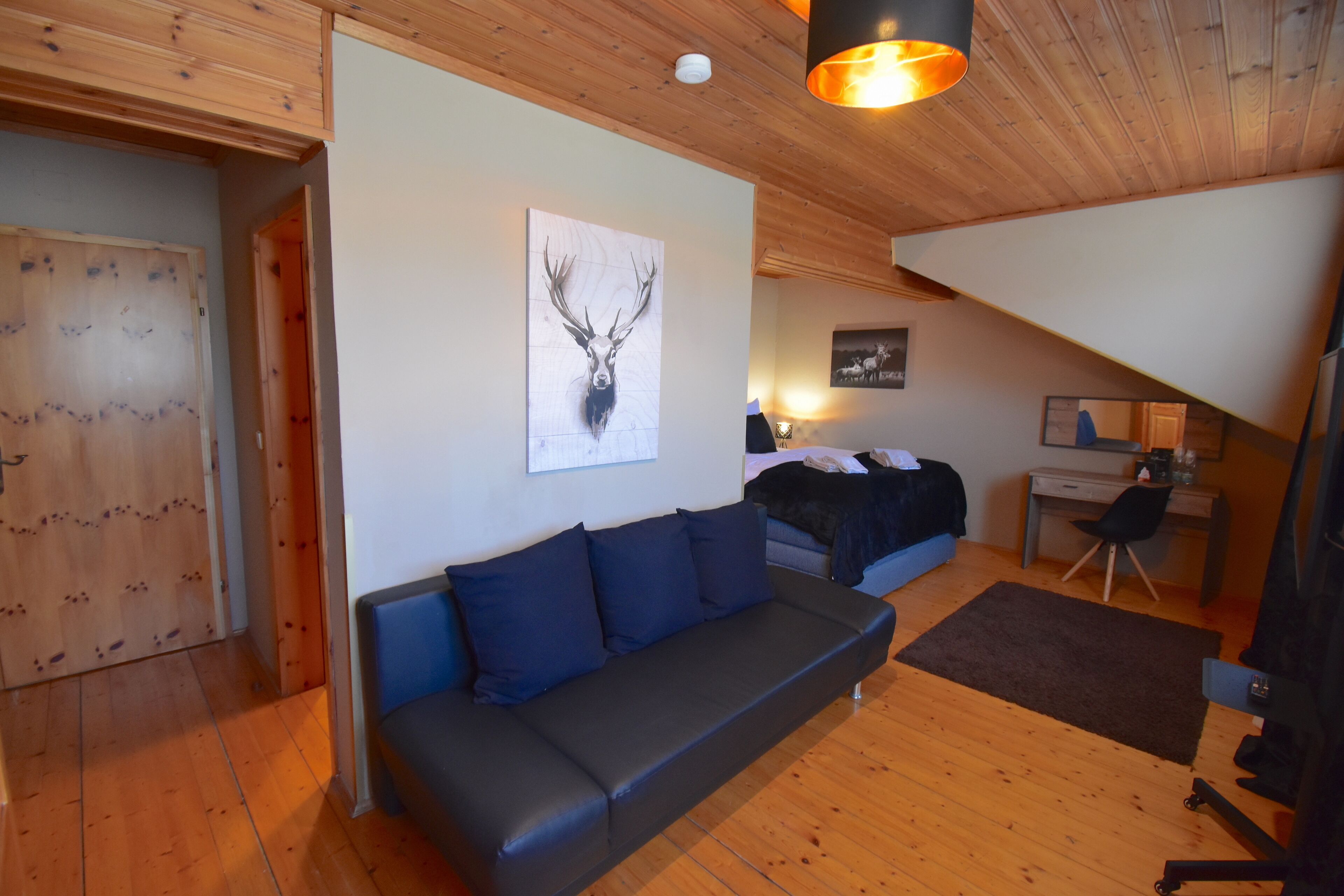 Una habitación acogedora con techo de madera, un sofá negro, una cama y un escritorio con una silla.