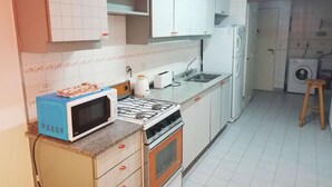A compact kitchen with a microwave, stove, sink, and a washing machine. - Recoleta Apartment - 2 Dormitorios (Buenos Aires)