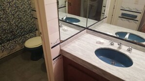 A bathroom with a toilet, a sink with a mirror, and a tiled wall. - Recoleta Apartment - 2 Dormitorios (Buenos Aires)