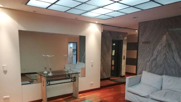 A modern living room with a glass coffee table, a white sofa, and a marble wall. - Recoleta Apartment - 2 Dormitorios (Buenos Aires)