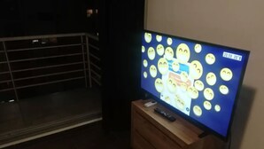 A television displaying a cartoon with various emoticons, a remote control, and a wooden cabinet below it. - Palermo Soho Apartment 2 (Buenos Aires)