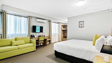 A hotel room with a bed, a green sofa, a desk with a chair, a television, and a wardrobe.