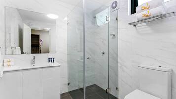 Un baño moderno con ducha de vidrio, un lavabo blanco con artículos de aseo y un inodoro blanco.