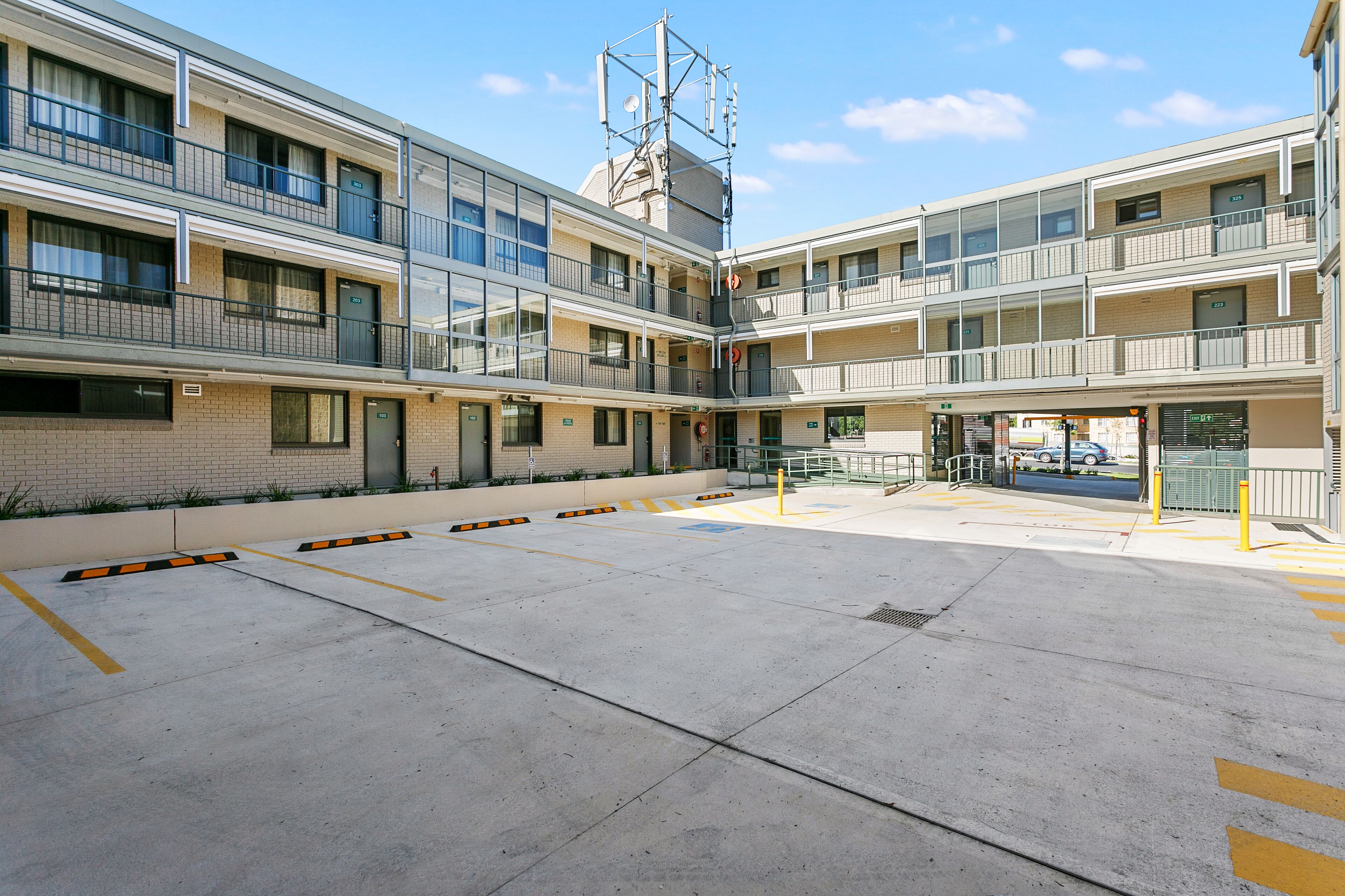 Un hotel de varios pisos con un patio central, varios balcones y un área de estacionamiento.