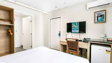 Hotelkamer met een bed, een bureau met stoel, een televisie en een kleine koelkast.