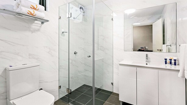 A modern bathroom with a glass-enclosed shower, a white toilet, a vanity with a mirror, and a towel rack.