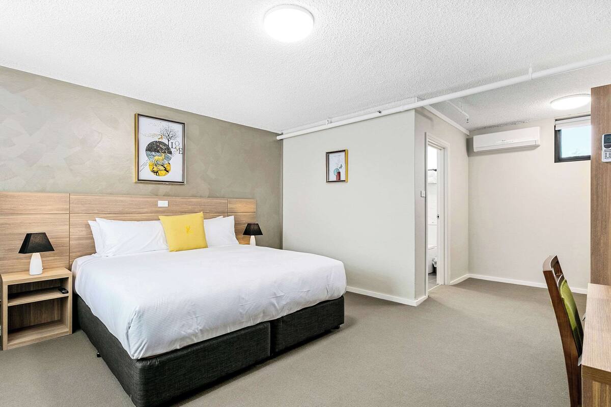 A bedroom with a bed, bedside tables, a chair, and a door leading to another room.