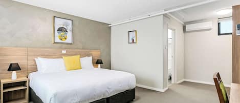 Un dormitorio con cama, mesitas de noche, una silla y una puerta que da a otra habitación.