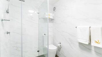Un baño con cabina de ducha de vidrio, inodoro y toallero con toallas.