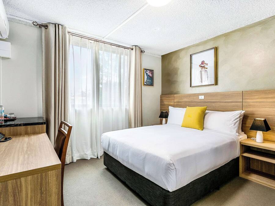 Una habitación de hotel con cama, mesita de noche, lámpara y escritorio con teléfono.