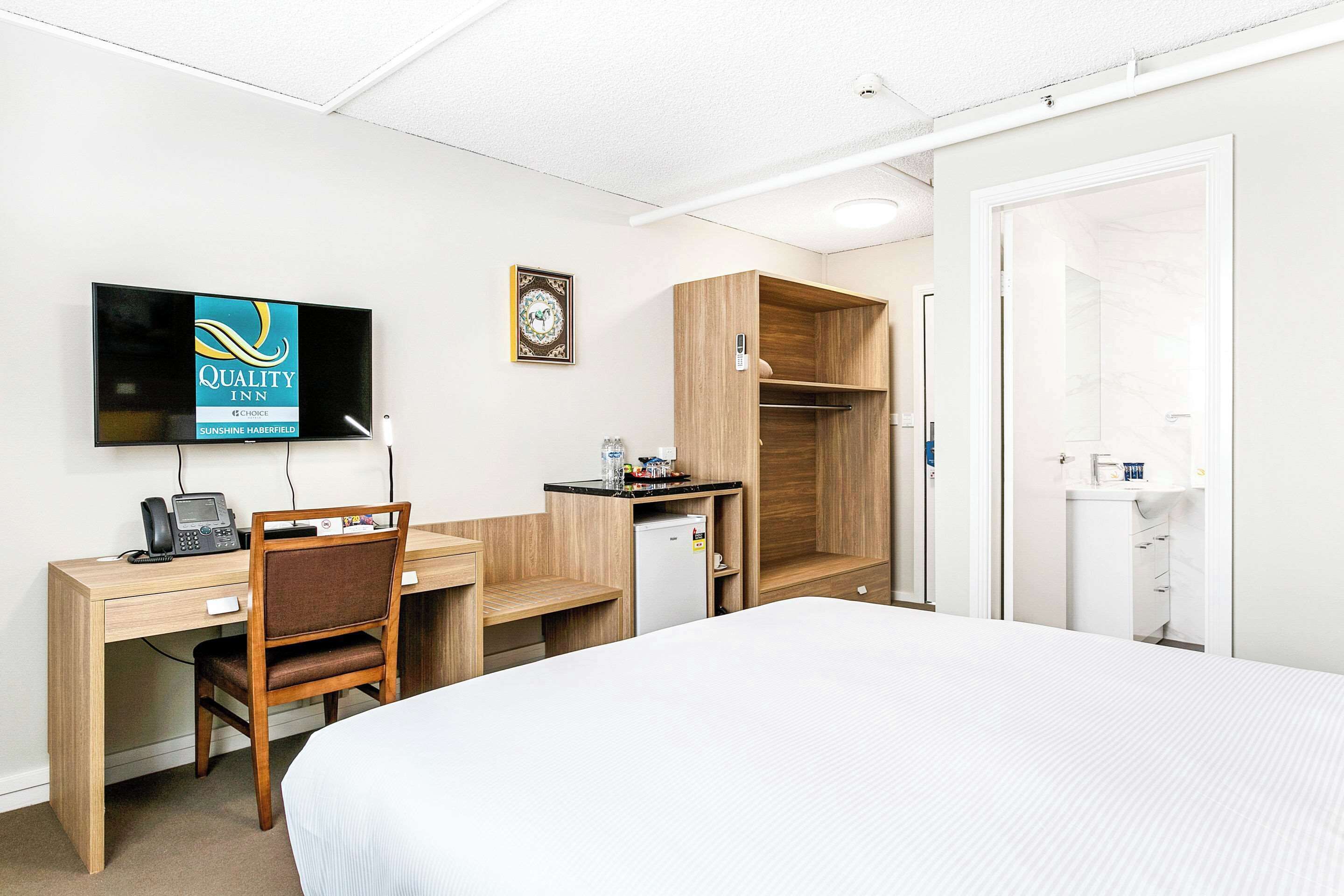 Une chambre d’hôtel équipée d’un lit, d’un bureau, d’une chaise, d’une télévision, d’une armoire et d’un petit réfrigérateur.