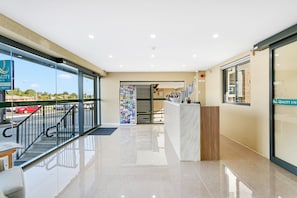 A hotel lobby with a reception desk, a staircase leading to an upper floor, and a large glass window offering a view of the street. - Quality Inn Sunshine Haberfield (Haberfield)