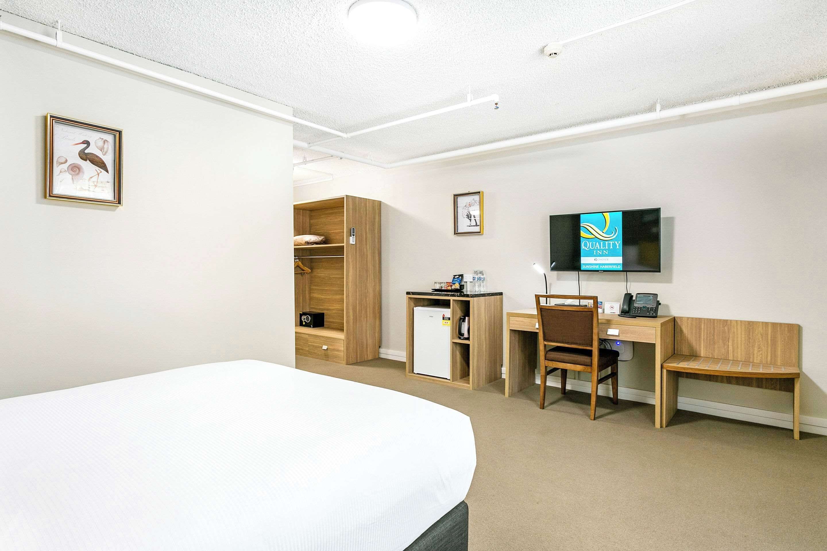 A hotel room with a bed, a desk, a chair, a television, and a wardrobe.