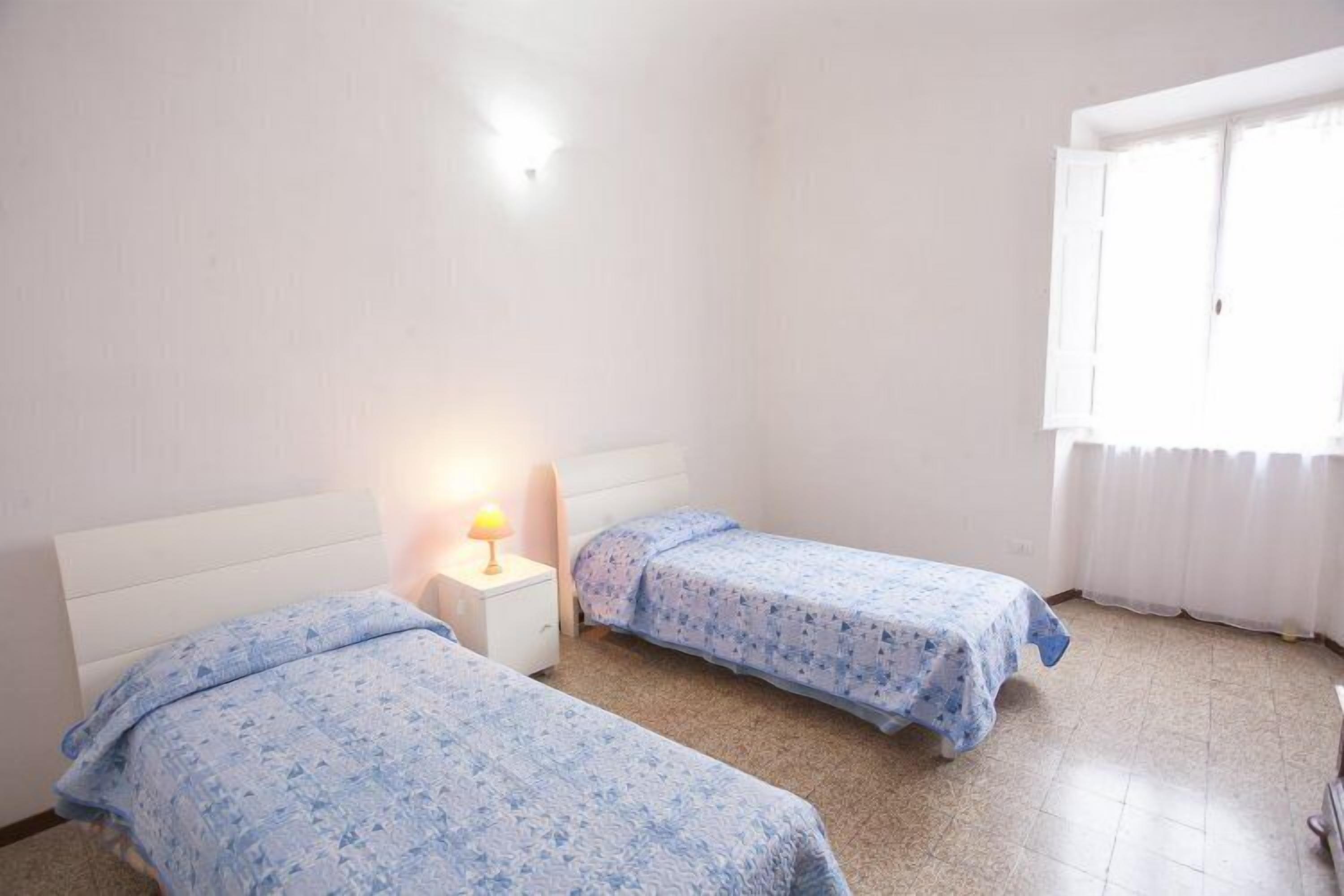 Une chambre avec deux lits simples, une table de chevet avec une lampe et une fenêtre avec des rideaux.