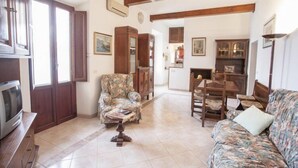A living room with a sofa, armchair, wooden coffee table, and a television. There are wooden beams on the ceiling and a door leading to another room. - Appartamenti La Calata (Portoferraio)
