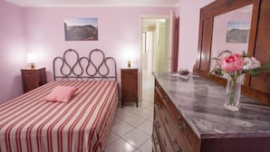A bedroom with a bed, a dresser, a mirror, and a vase with flowers. - Casa Malva (Portoferraio)