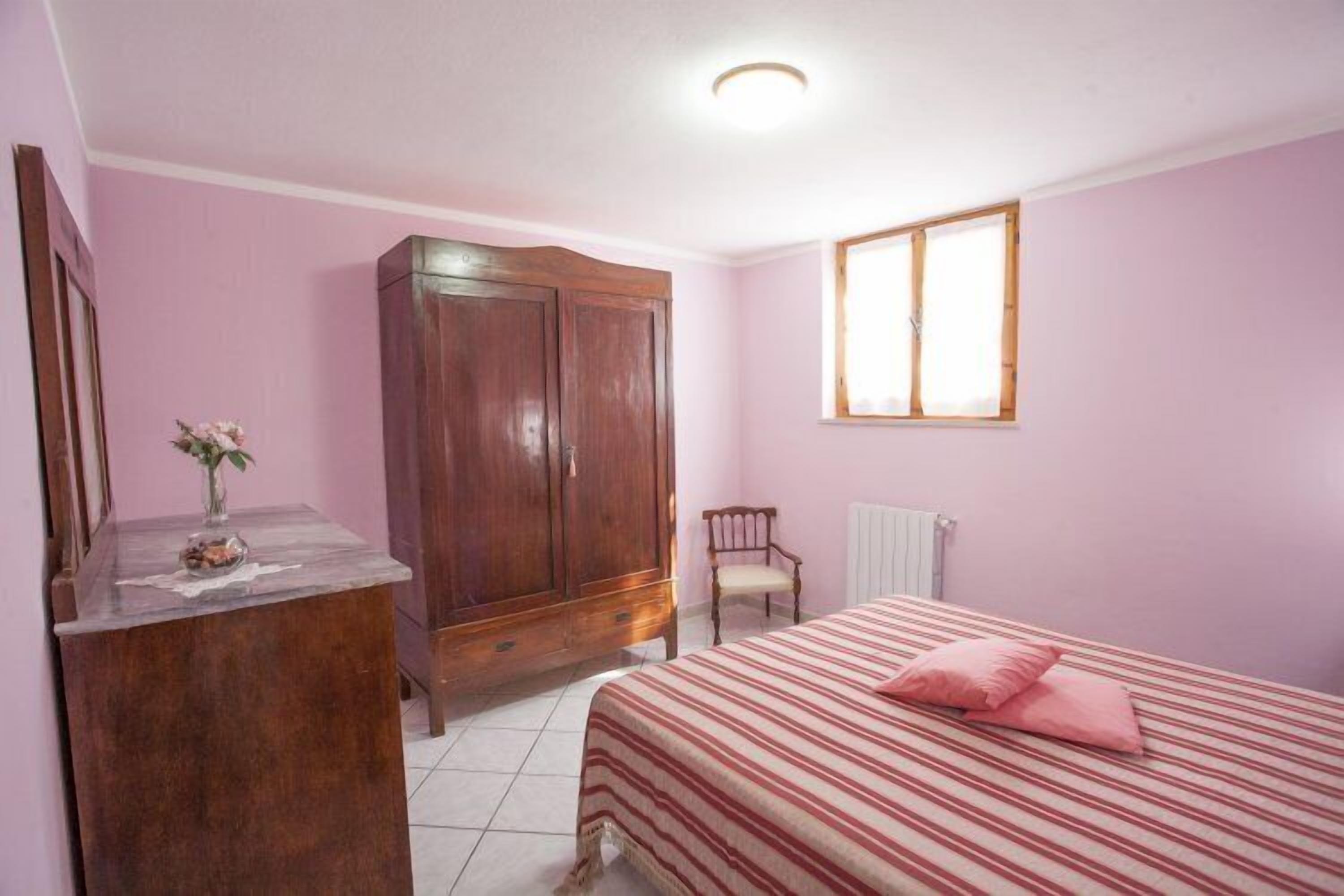 A bedroom with a bed, a wooden wardrobe, a chair, and a window.