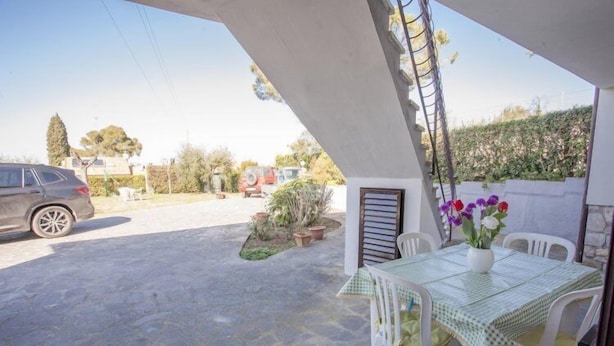 A covered outdoor area with a table and chairs, a parked car, and potted plants. - Casa Malva (Portoferraio)