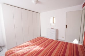 Un dormitorio con edredón a rayas, cómoda, espejo y armario.