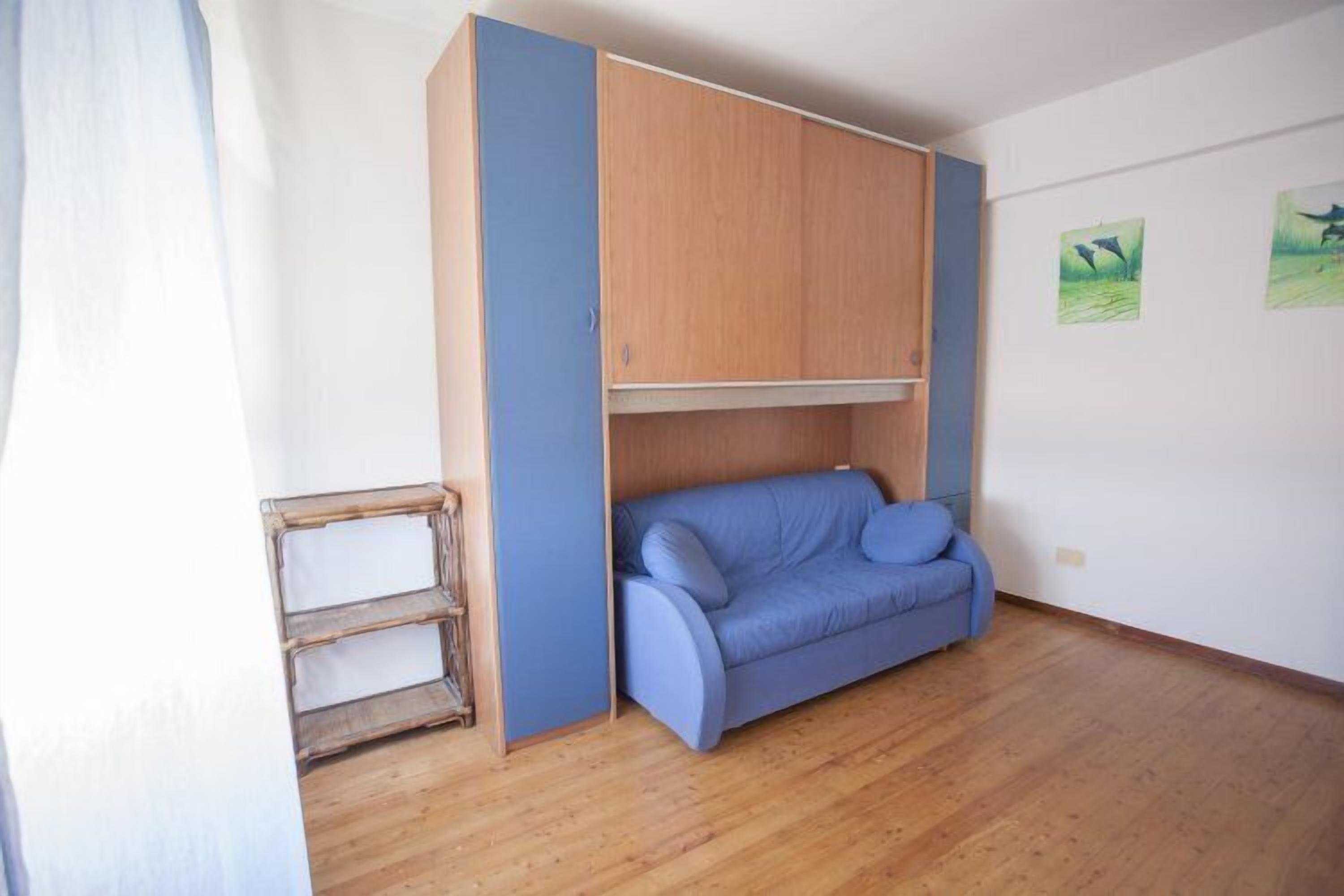 A room with a blue sofa, wooden wardrobe, and a small wooden ladder.