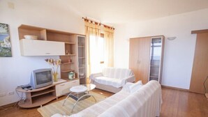 A small, well-lit room with a sofa, a chair, a TV on a wooden stand, and a cabinet with shelves. - Scoglietto (Portoferraio)