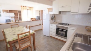 A compact kitchen with white cabinets, a dining table with chairs, a refrigerator, an oven, and a sink. - Scoglietto (Portoferraio)