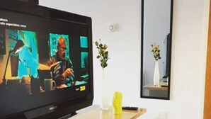 A television on a wooden stand with a remote control, a vase with flowers, and a mirror on the wall. - Paraguay & Salguero - Energy Home (Buenos Aires)