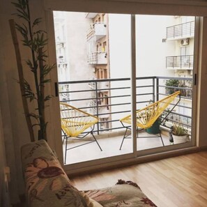 A room with a sofa, two yellow chairs, a large window, and a bamboo plant.