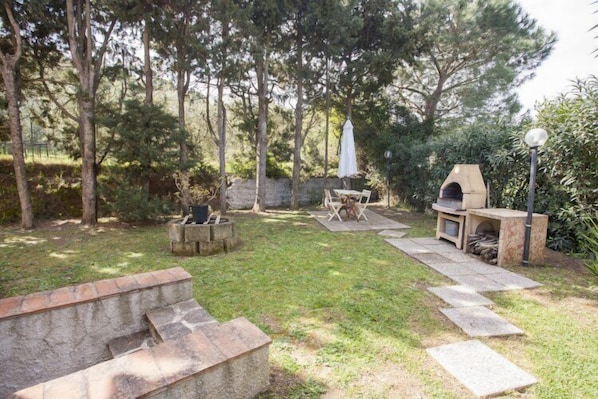 A backyard with a stone bench, a fire pit, a barbecue grill, and a paved pathway.