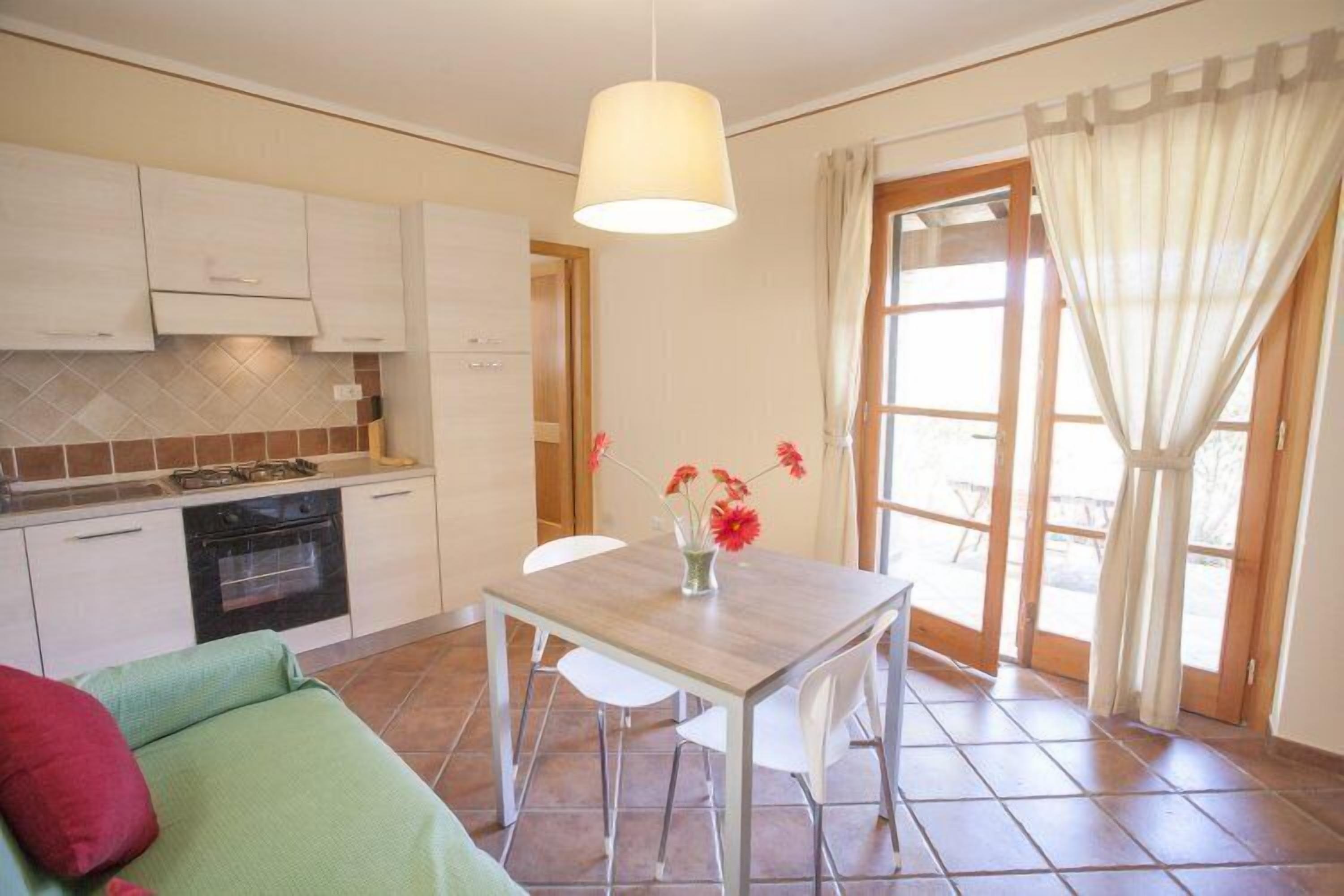 A compact kitchen with white cabinets, a wooden table, and a dining area.