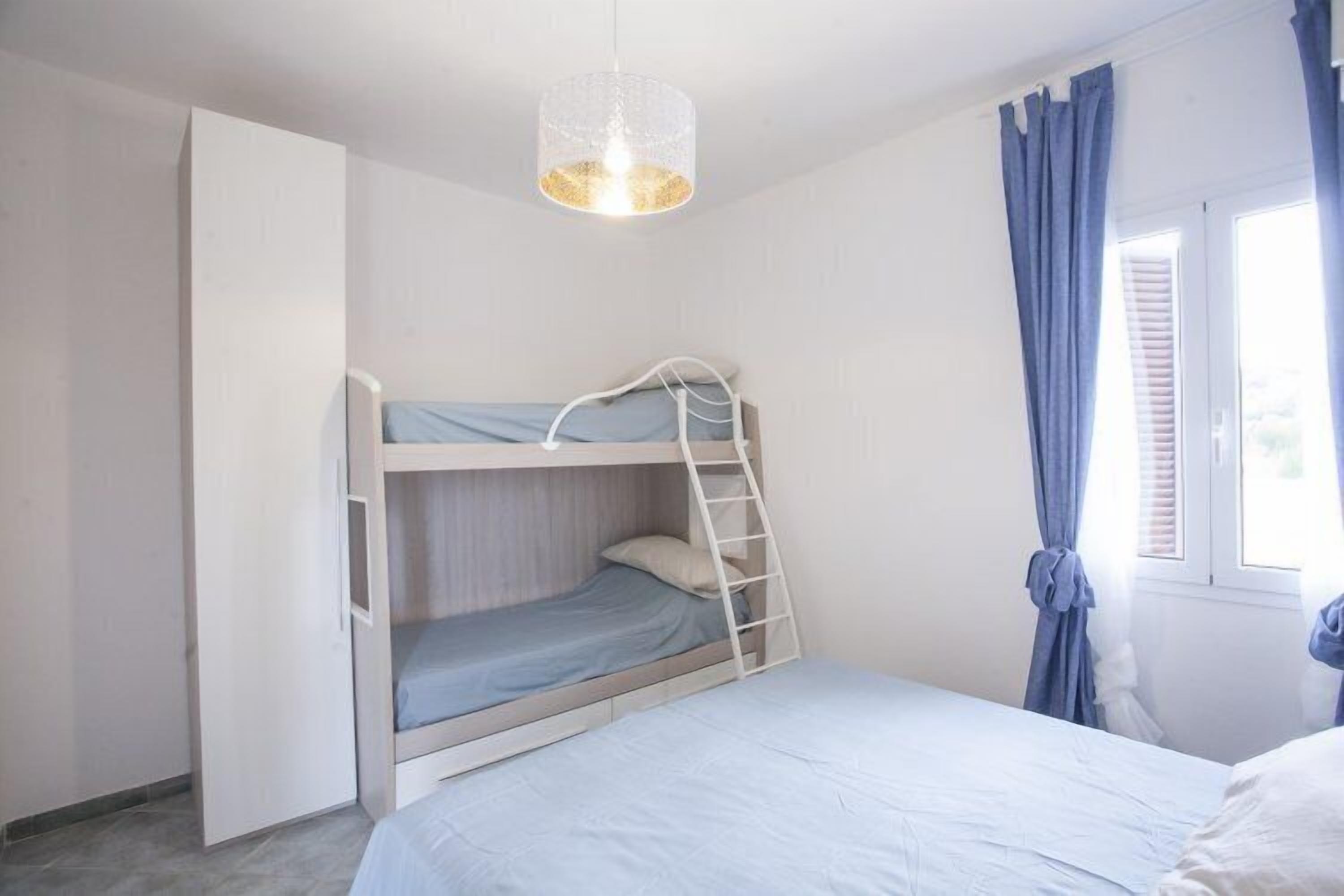 Quarto com cama beliche, escada, janela com cortinas e luminária pendente.
