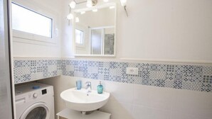 A bathroom with a washing machine, sink, and a mirror with lights. - Bilocale Koala (Capoliveri)