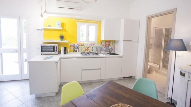 A compact kitchen with white cabinets, a microwave, and a colorful backsplash. - Bilocale Koala (Capoliveri)