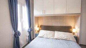 A bedroom with a bed, curtains, a nightstand, a lamp, and a wardrobe. - Bilocale Koala (Capoliveri)