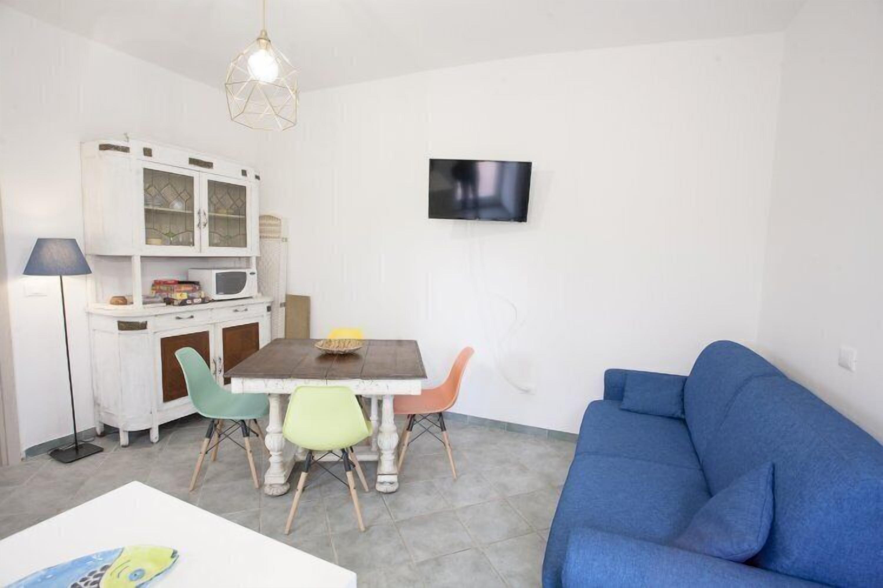 Ein kompakter Wohnbereich mit Essplatz, einem blauen Sofa, einem Flachbildfernseher und einer weißen Schrank mit Glastüren.