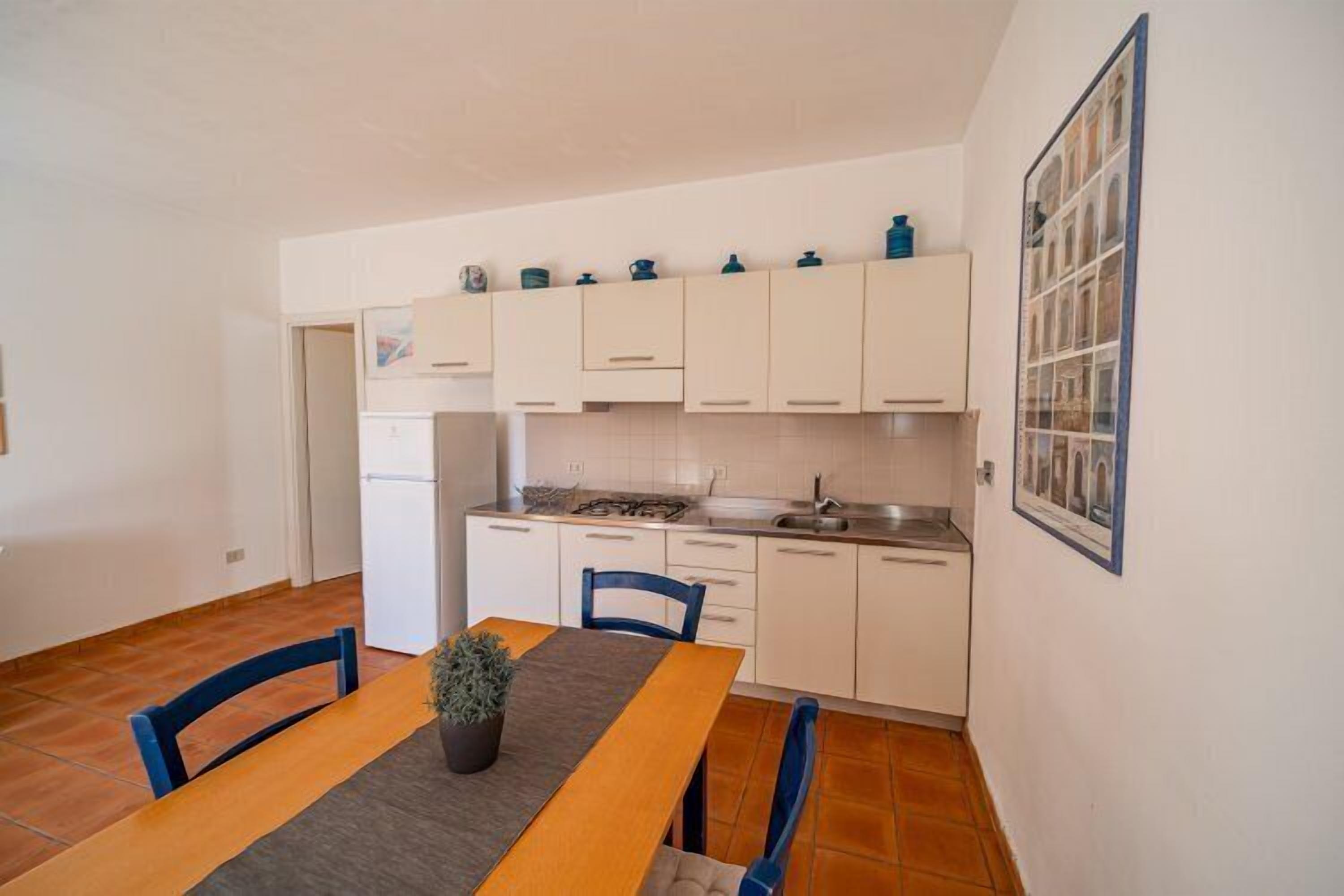 A compact kitchen with white cabinets, a dining table with chairs, and a small potted plant.