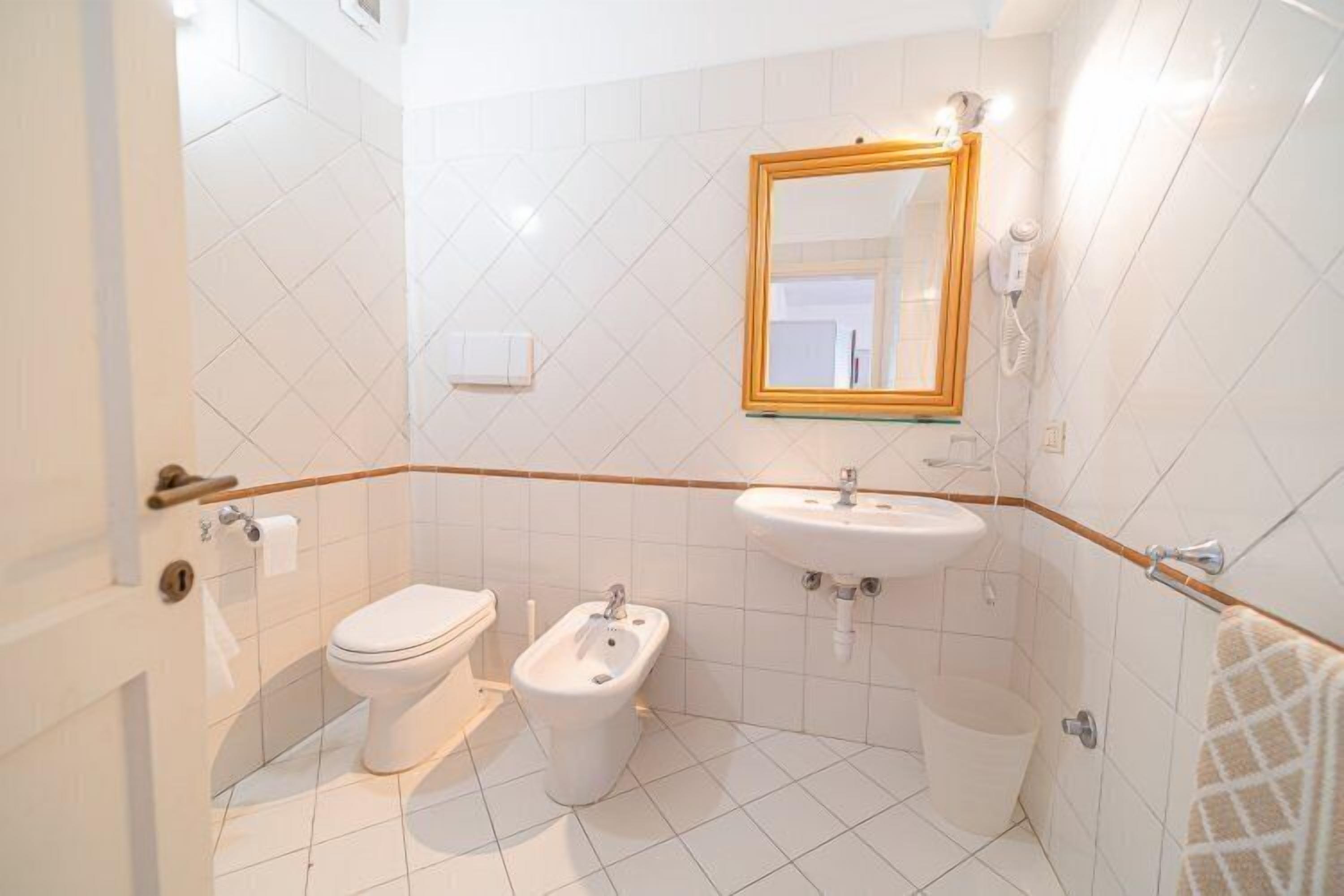A bathroom with a toilet, bidet, sink, and mirror.