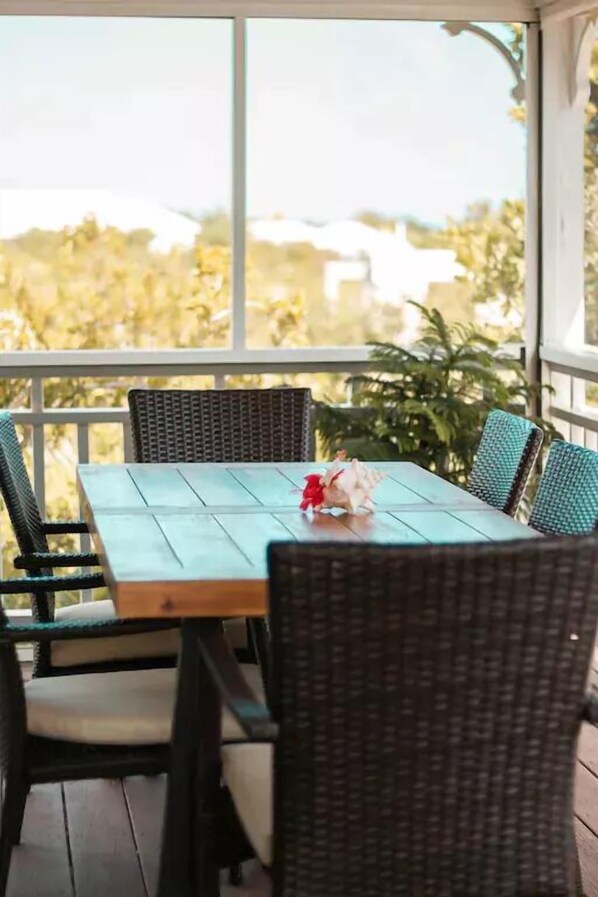 Un porche cubierto con una mesa de madera y sillas de mimbre, con vistas a un jardín.