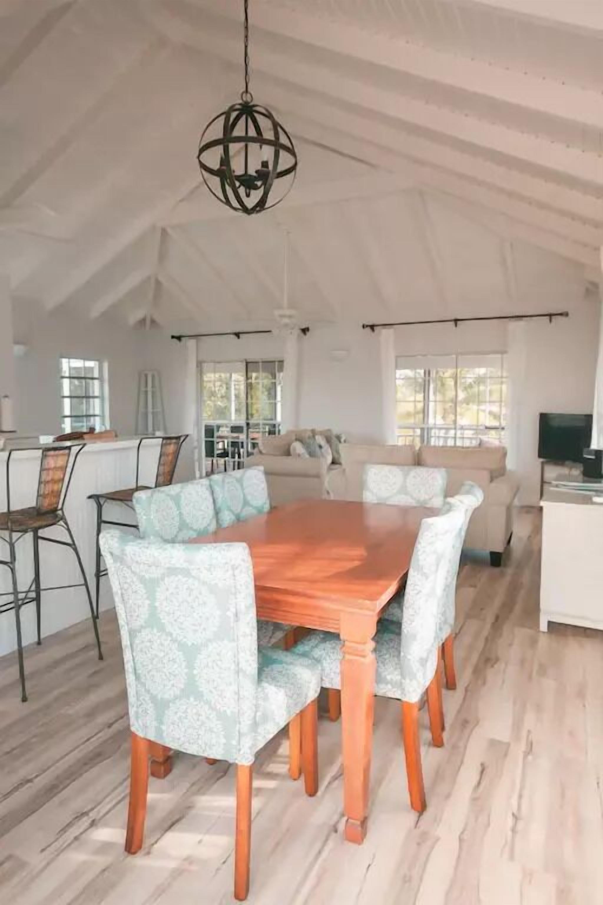 Un comedor amplio con una mesa de madera y sillas estampadas, un colgante de luz y vistas a la cocina y al salón.