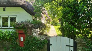 A quaint cottage with a thatched roof, a stone wall, and a red mailbox. - Thatched Eaves (Ringwood)