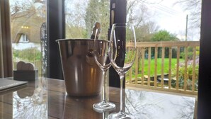 A table with two champagne flutes and a metal bucket, likely containing champagne, in a room with a view of a wooden deck and greenery outside. - Thatched Eaves (Ringwood)