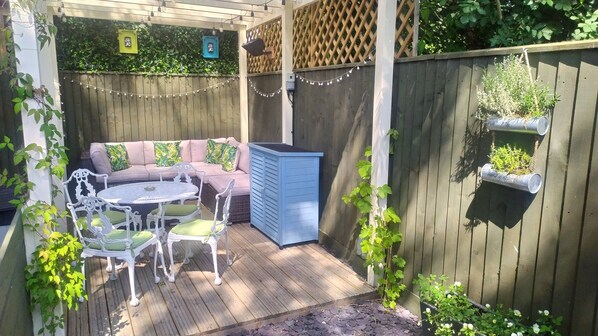 A wooden deck with a seating area, including a table and chairs, and a blue storage unit.